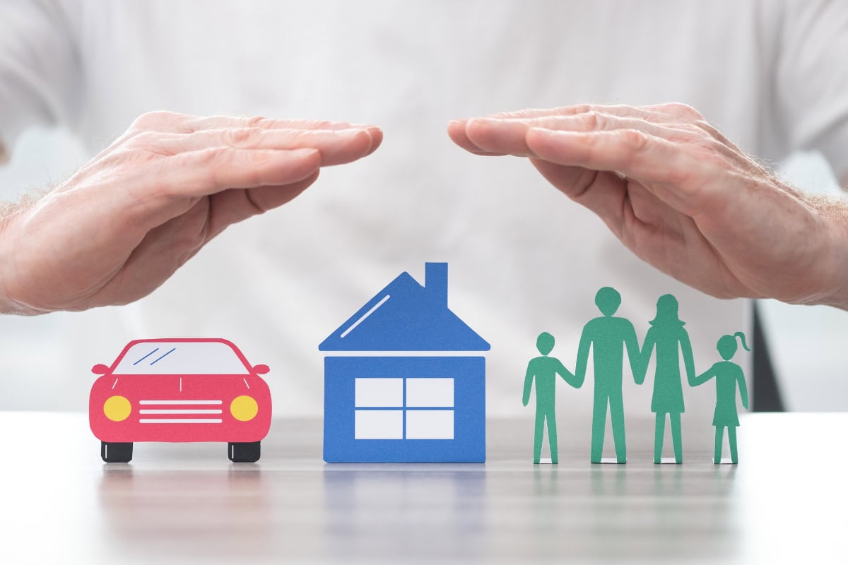 Manos protegiendo una casa, un coche y una familia